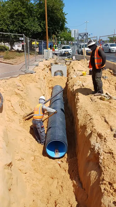 הנחת צינור בקוטר גדול בתעלה עמוקה, עם עובדים בתוך החפירה ומעליה.
