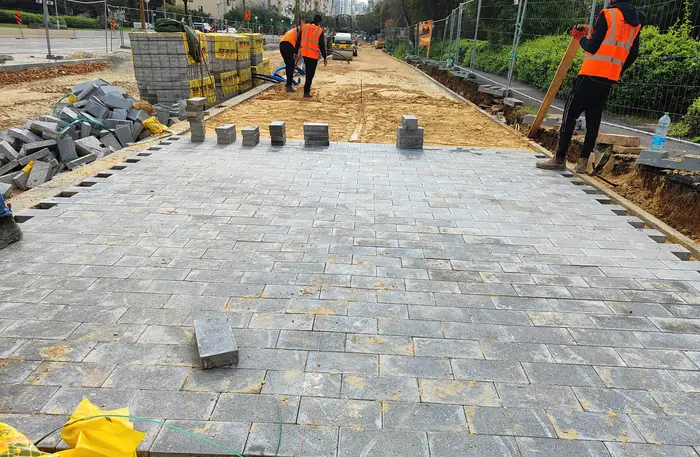 ריצוף באבן משתלבת: עובדים מרצפים משטח, עם ערימות אבן מוכנות בצדדים.
