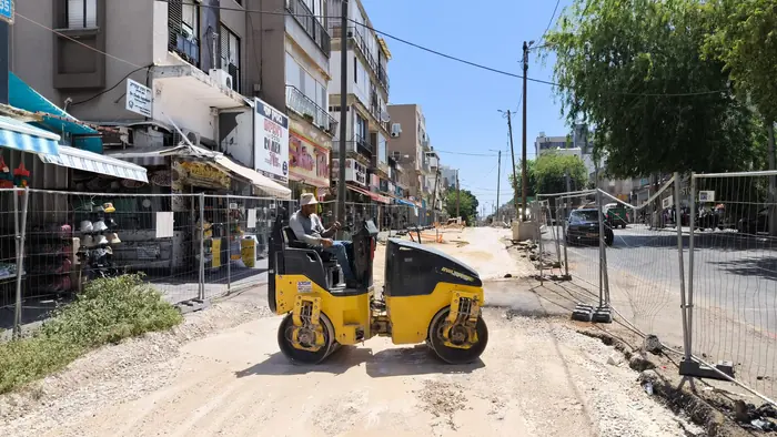 הידוק שכבה במכבש ברחוב מסחרי פעיל, כשהחנויות פתוחות משני הצדדים.