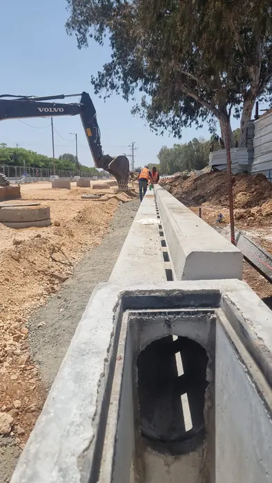 הנחת מעביר מים מבטון טרום בתוואי, לצד אבני שפה ומחפרון.