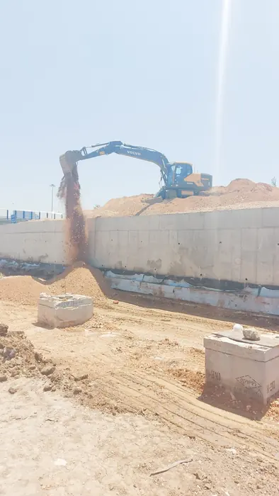 עבודות עפר לצד קיר תומך יצוק: מחפרון פורק חומר בתוואי.