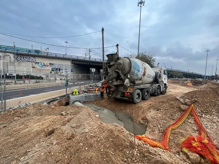 יציקת בטון במקטע G1-7 של הקו הירוק: מערבל פורק לתוך התבנית, צוות עובדים בחפירה ואלמנטי ניקוז לצדה.