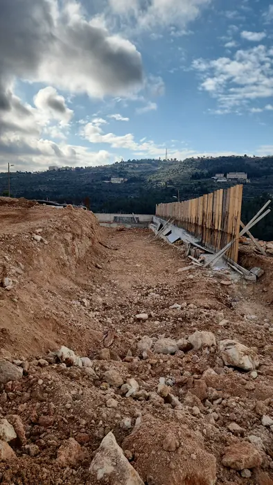 עבודות עפר בפארק הרוגם: קיר תמך מדופן בלוחות פלדה לצד קרקע חפורה, על רקע נוף ההרים.