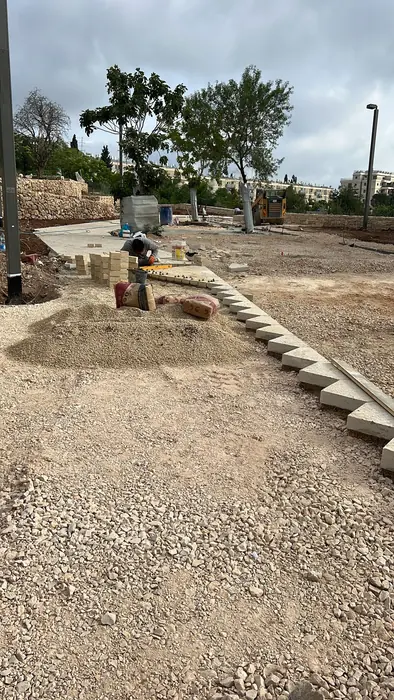 בניית קיר ישיבה מאבן בקשת לאורך שביל הפארק, כשהשטח סביבו עדיין בעבודה.