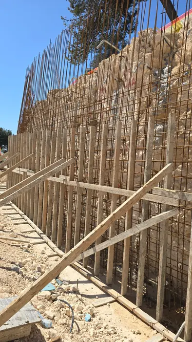 כלוב זיון ותבניות לקיר בטון הנשען על חזית הסלע.