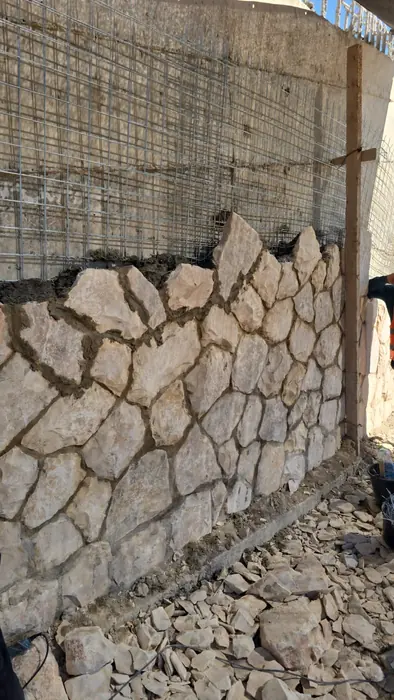 בניית חיפוי אבן לקיר תומך, עם רשת זיון להמשך הבנייה מעליו.