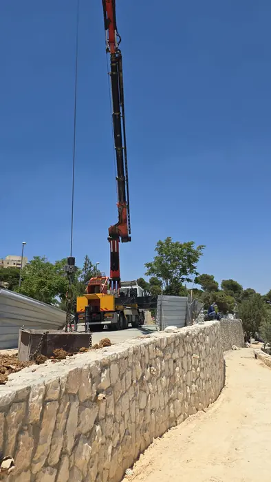 מנוף עובד מאחורי קיר האבן שהושלם, בשלב מתקדם של הפיתוח.