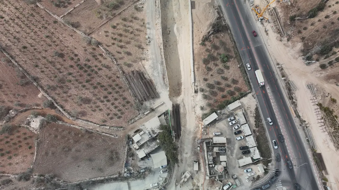 אתר התארגנות לאורך הכביש: ערימות צנרת, תוואי תעלה בחפירה, מבני אתר ומנוף.